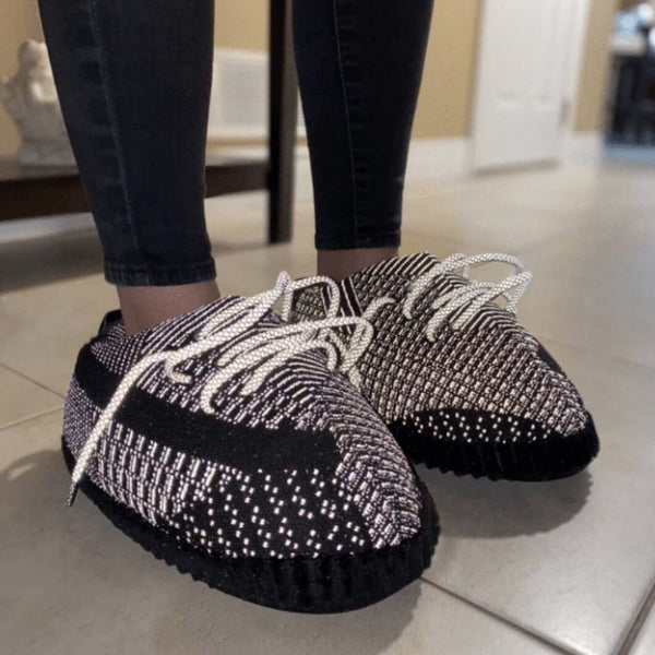 A lifestyle shot of someone wearing the slippers indoors, illustrating their versatility for both indoor and outdoor use. A promotional banner in the corner displays the offer for 50% off the second pair with code HALFOFF.